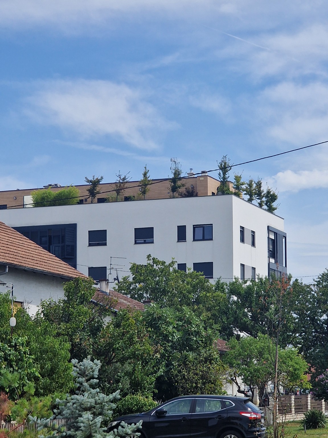 Pogled iz ulice na stambenu zgradu sa stablima na krovnoj terasi.